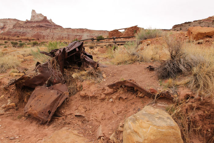 A car buried in a wash with cabin ruins and Temple Mountain in the background.