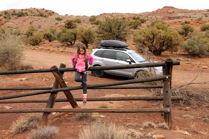 A child on a wooden fence next to a parked car along a dirt road in the San Rafael Swell, Utah.