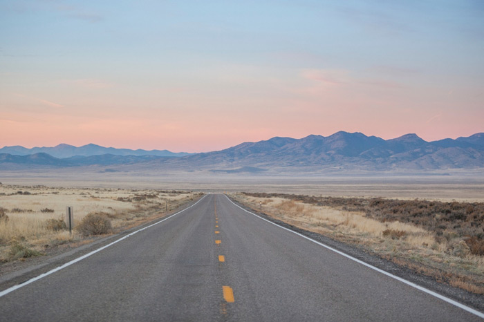 A highway through the Nevada desert with views of the towering mountains of Great Basin National Park ahead.