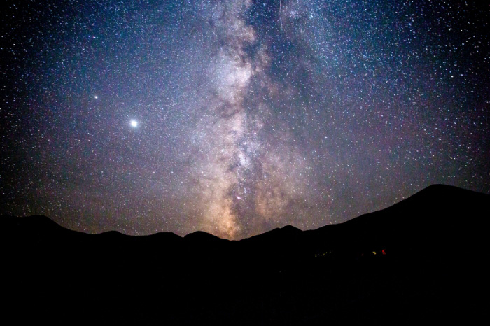 Nighttime skies in Great Basin National Park showing Milky Way rising over the dark mountainous landscape of the park.