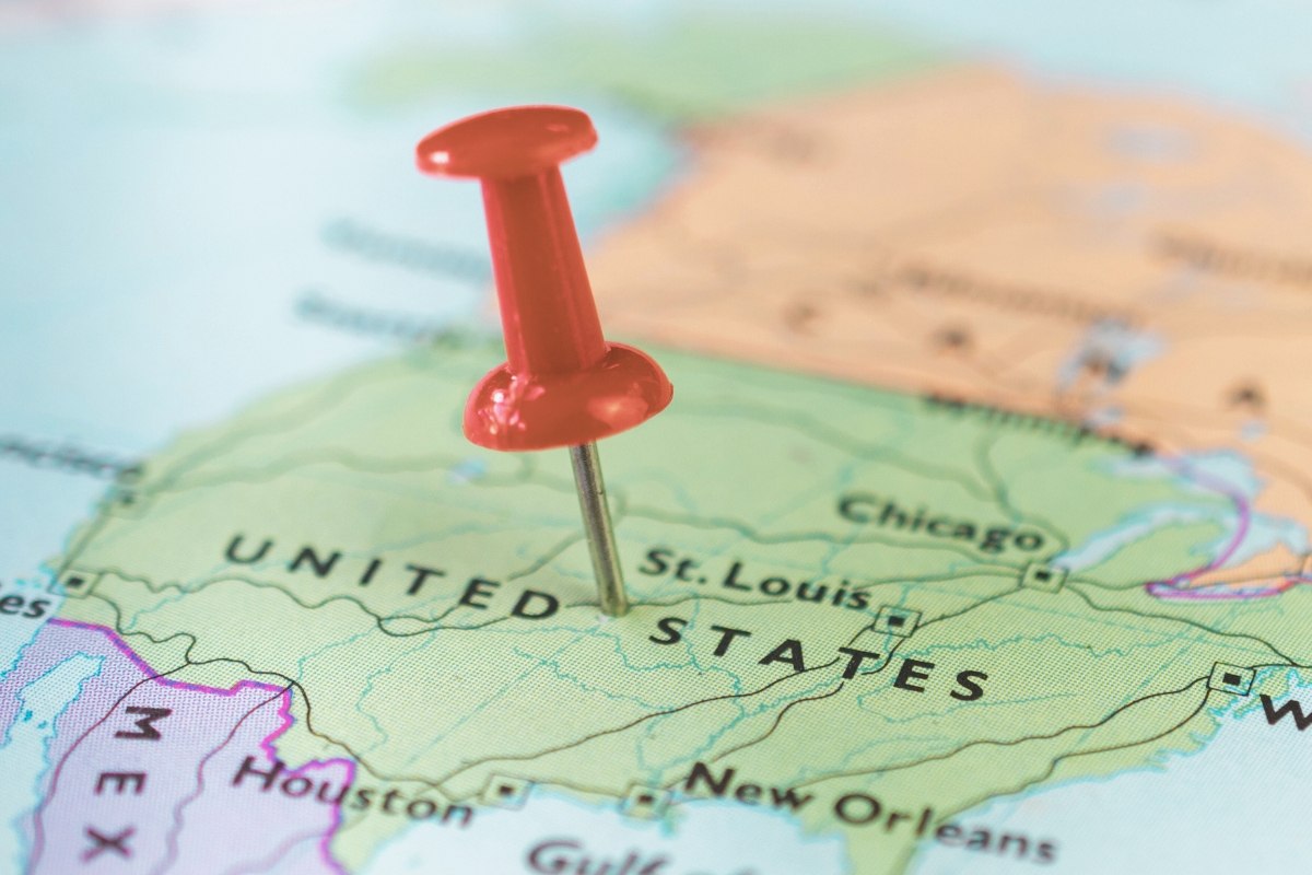 A printed map of North America with USA marked green and a red pin in the middle of the country, marking a travel destination.
