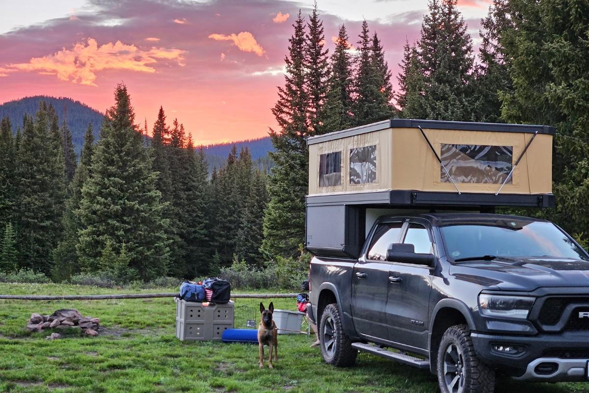 A beautiful colorful sunset in the high Colorado mountains with a truck camper in the view, parked for the night, and lush green trees just behind it.