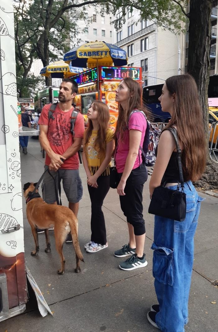 A family with two young daughters and a dog, standing on a New York City street in front of a food truck