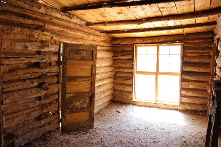 Interior of the Josie Morris Cabin in Dinosaur National Monument, Utah, showing log walls, dirt floors, and a window letting in natural light.
