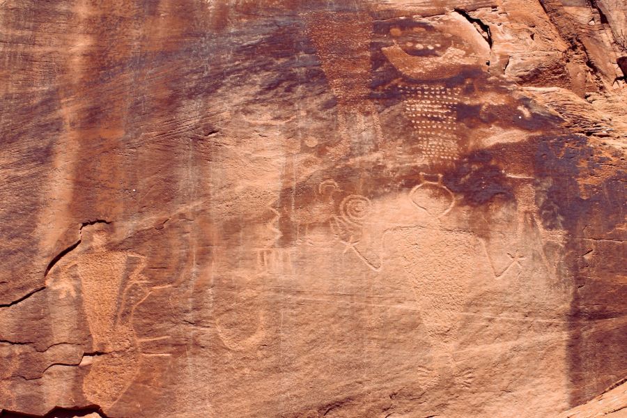 Close-up of the Cub Creek Petroglyphs panel showing multiple Fremont-era carvings, including human figures, animals, and dotted geometric patterns etched into darkened sandstone.