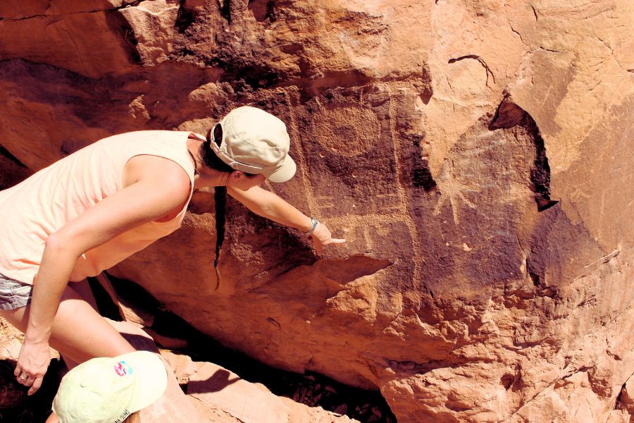 Visitor pointing toward a prominent human-like figure with clearly defined body features, carved into the sandstone with desert varnish.