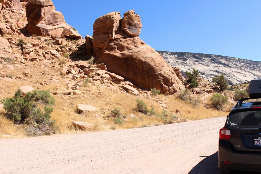 View of the Cub Creek Petroglyphs site from the parking area along Cub Creek Road, showing the car and the main panel of Fremont rock art visible a short distance away.