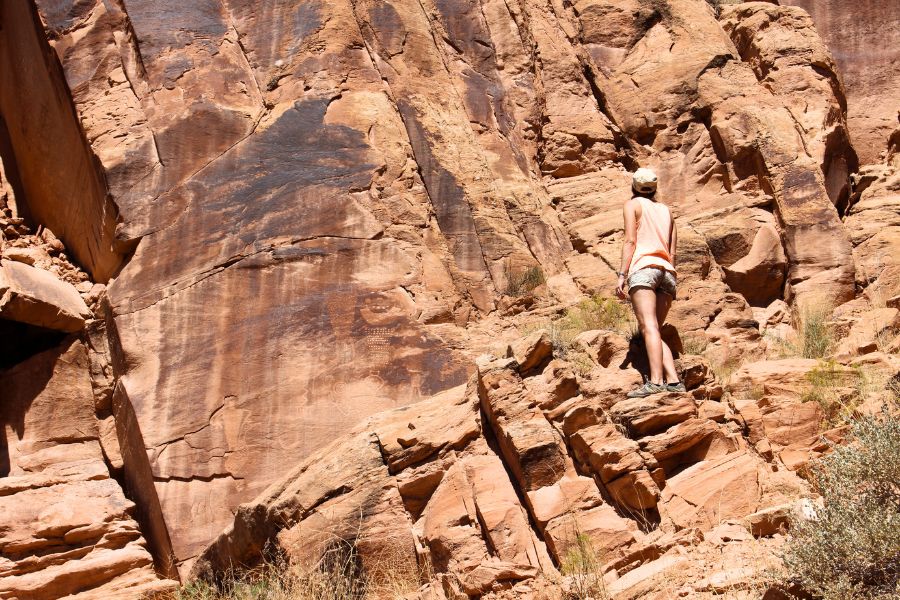 Visitor standing on sandstone rocks at Cub Creek Petroglyphs in Dinosaur National Monument, Utah, scanning the cliff face for more Fremont carvings.