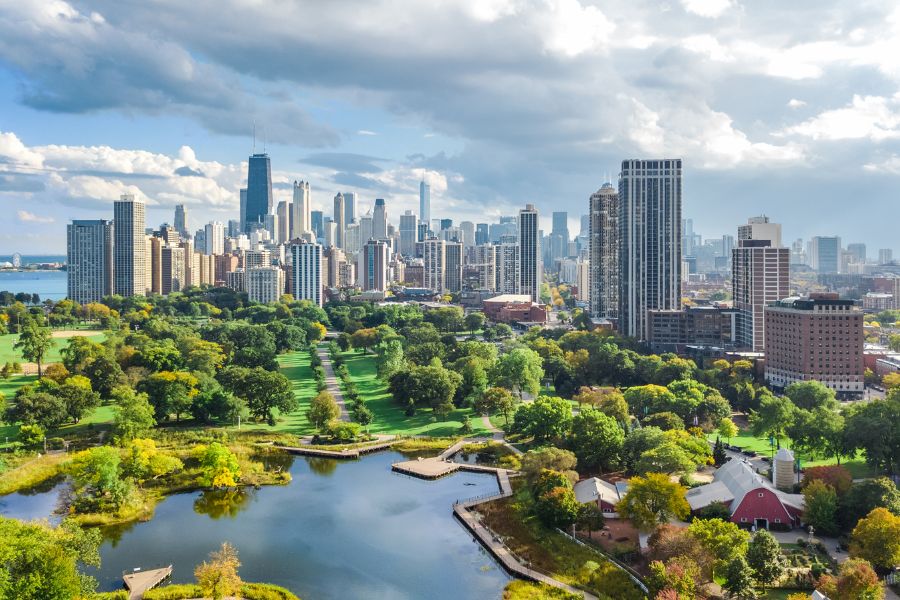Aerial view of Lincoln Park in Chicago with greenery, pond, zoo buildings, and city skyline in the background.