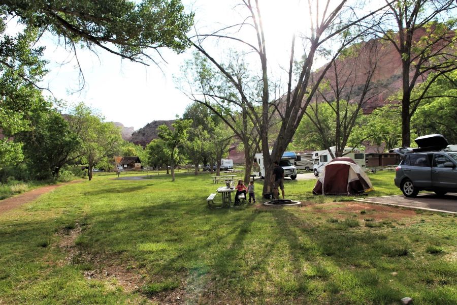 Tent, car, and RVs at Fruita Campground in Capitol Reef National Park, on a large grassy field and with the Fruita Trail running along the edge.