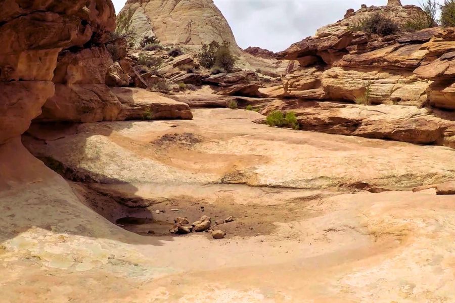 Dry water basin in the slickrock along the Tanks spur of Capitol Gorge Trail, with rocky walls on both sides and ahead, showing the natural erosion of rainwater reservoirs