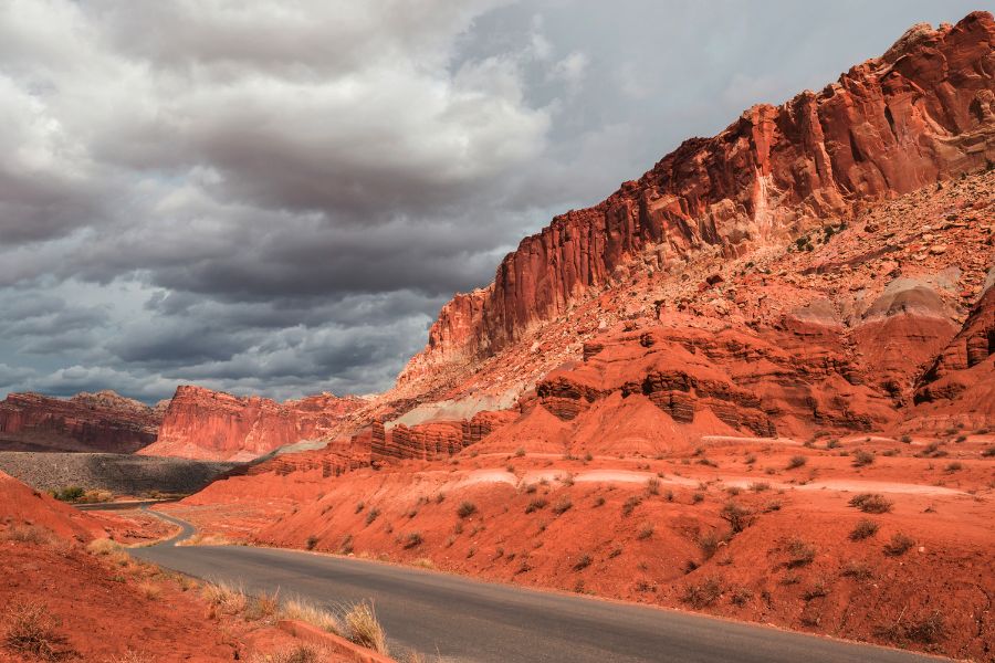 Capitol Reef Scenic Drive with a paved road winding through the park, as towering Waterpocket Fold cliffs and rock formations rise along the right side on the return toward the Visitor Center.