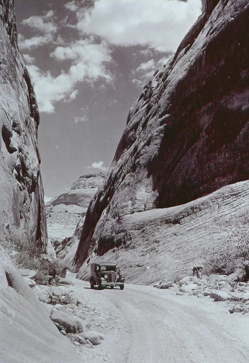 A historic black-and-white image of a car going through the narrow Capitol Gorge.