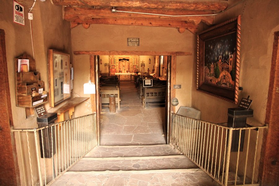 Stone steps and wooden beams framing the entrance to the Our Lord of Esquipulas chapel, leading into a softly lit shrine with pews.
