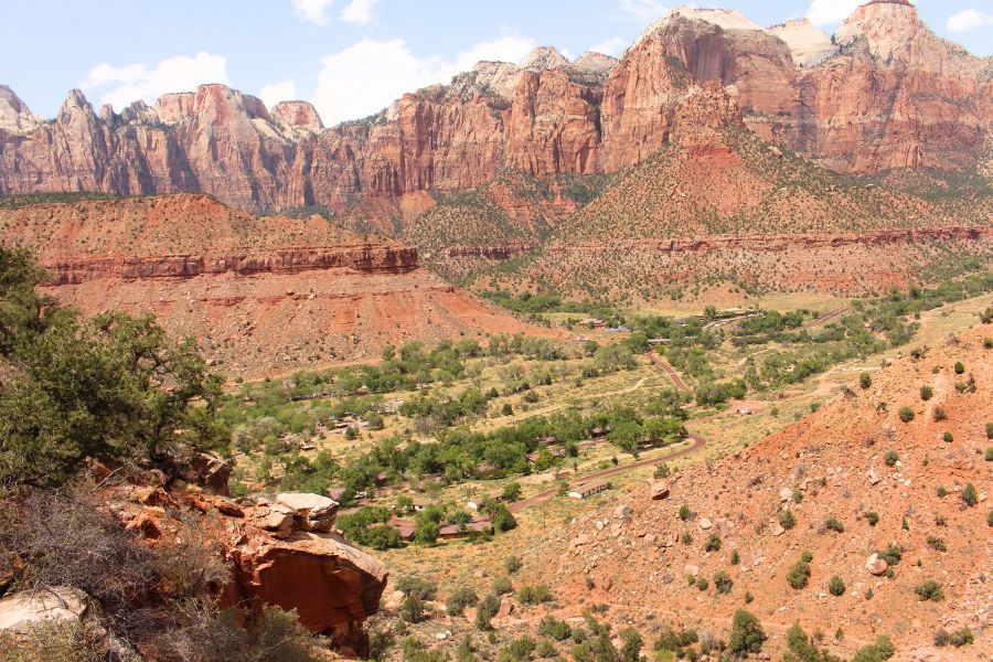 Wide view of the valley below showing park roads, buildings, and sweeping red rock cliffs in the distance.
