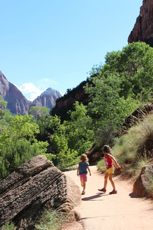Paved section of the Lower Emerald Pool Trail near Zion Lodge with children walking along a flat, open stretch surrounded by greenery.