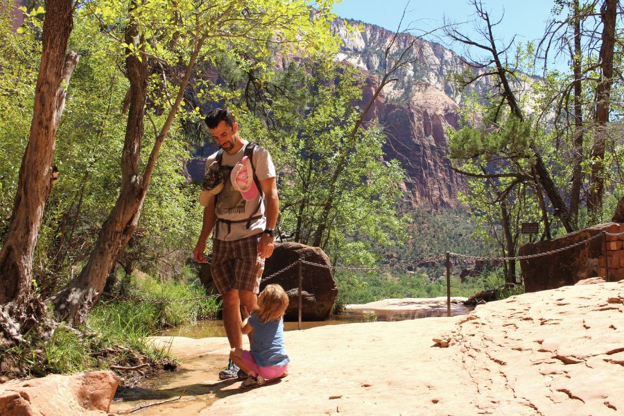 Father and child standing on slickrock near a chained overlook at Middle Emerald Pools with canyon views beyond.