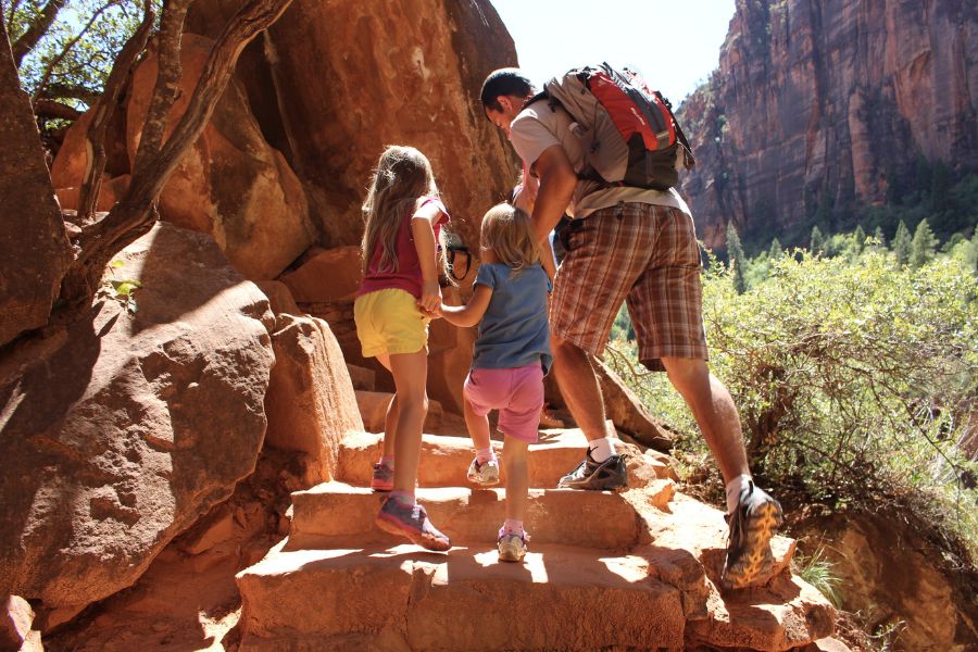Family hiking up rugged stone steps on the connector trail between Lower and Middle Emerald Pools with cliffs in the background.