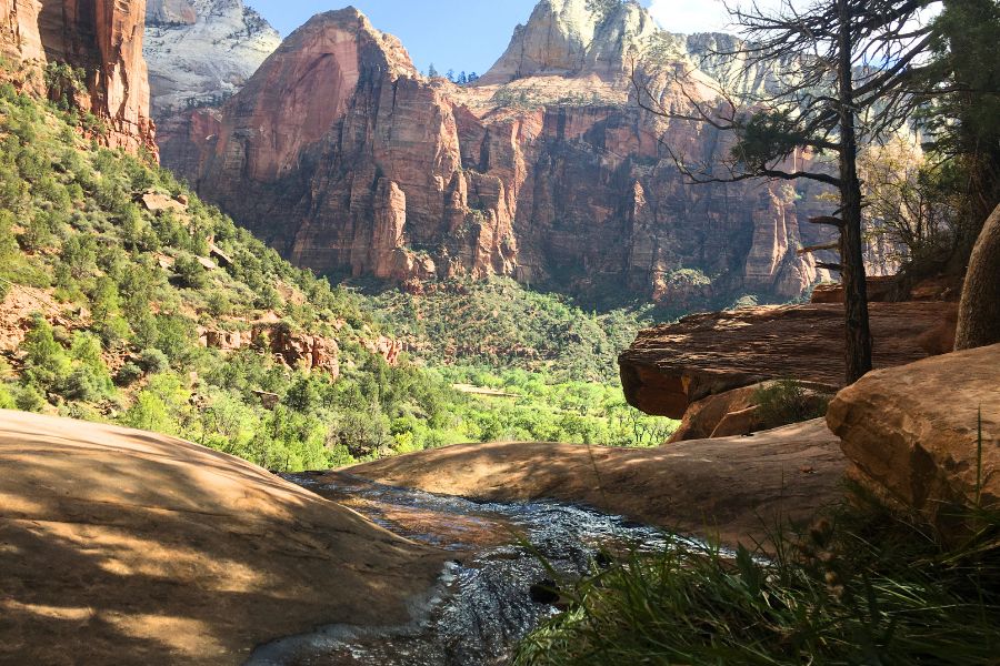 Water spilling over a sandstone ledge at Middle Emerald Pools with colorful canyon cliffs rising in the distance.