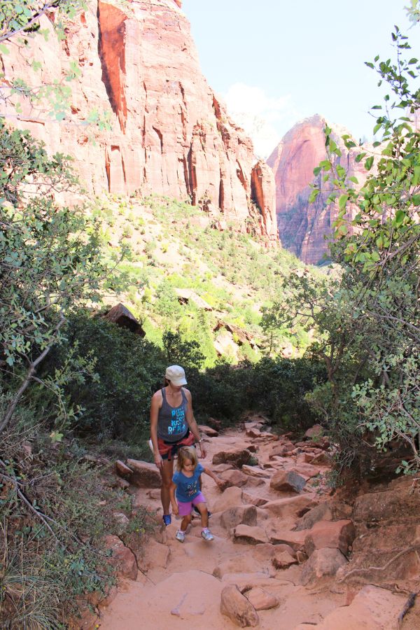 Hikers climbing the rocky and sandy Upper Emerald Pool Trail with canyon views in the background.
