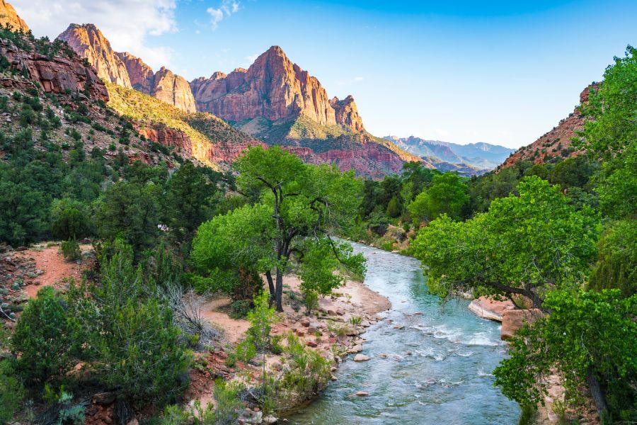 Sunset soon-to-arrive at Canyon Junction in Zion National Park, with the Virgin River flowing beneath the bridge and towering canyon cliffs glowing orange in the evening light — one of the best sunset views in Zion.