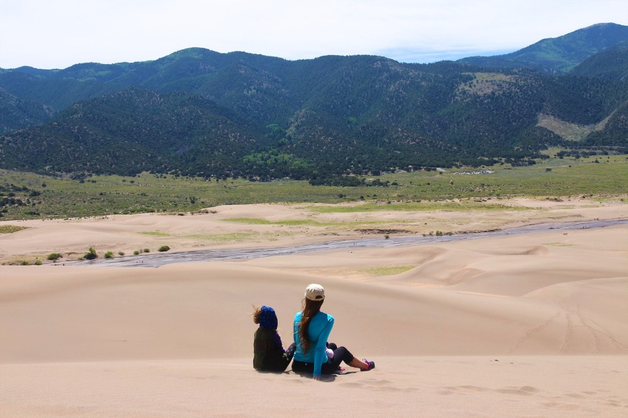 Family sitting high on the dunes overlooking green forested hills and Medano Creek below.