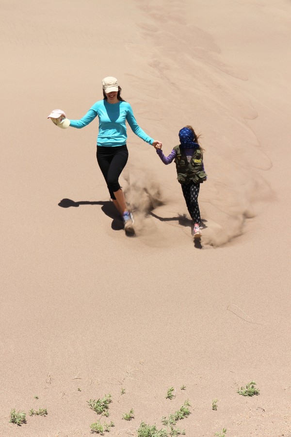 Mom and daughter running down a steep sand dune.