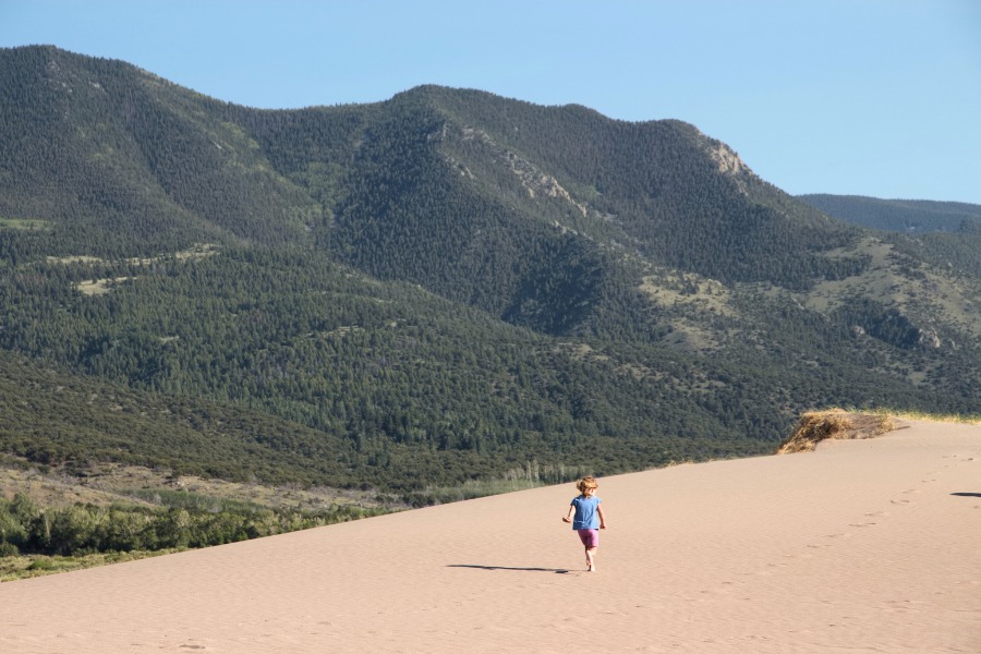A child walking on an expansive flat dunefield with classic Colorado mountains rising in the near background.