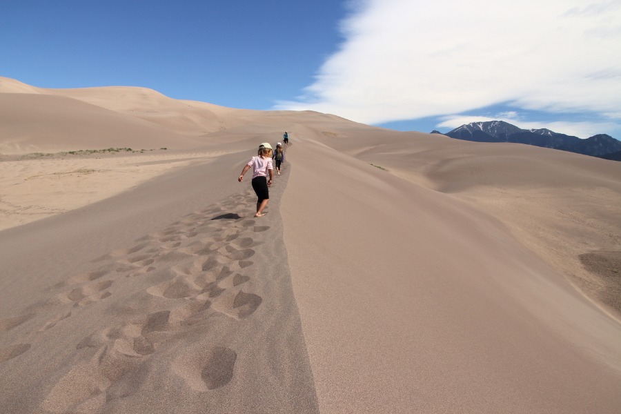 Family hiking on the expansive dunefield of Great Sand Dunes National Park backed by rugged mountain peaks.