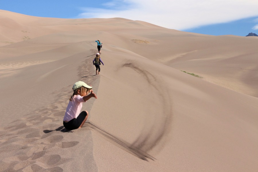 Family hiking along the dune ridge in Great Sand Dunes National Park, with one child throwing sand in the air with joy.