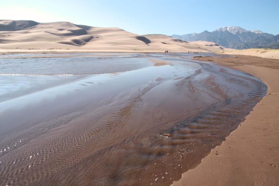 Medano Creek flowing gently at the base of the dunes with mountains in the background.