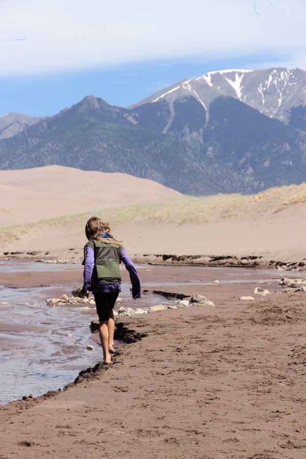 A child approaching the shallow Medano Creek, with dunes and mountains in the background.