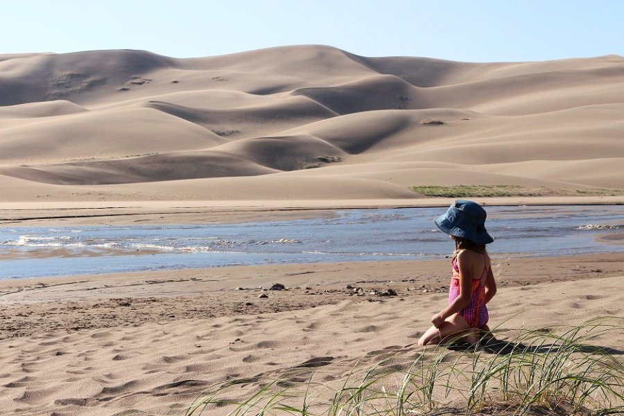 Child sitting on the sandy shore of seasonal Medano Creek, flowing at the base of the Great Sand Dunes National Park dunefield.