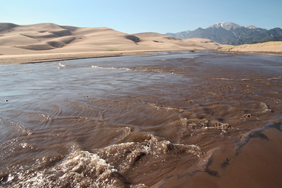 Medano Creek flowing swiftly at the base of the dunes in Great Sand Dunes National Park with mountains in the background.