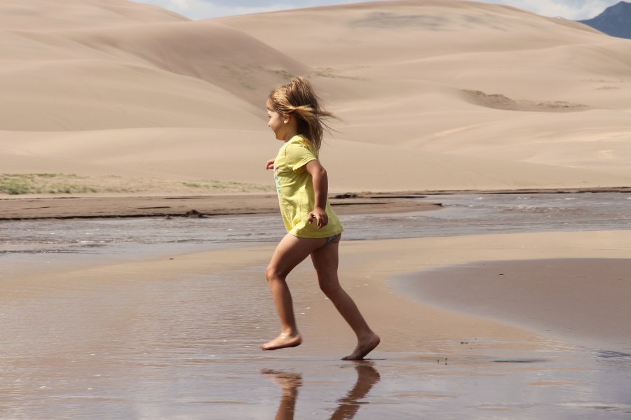 Child running through the shallow Medano Creek, with dunes rising just behind the water.