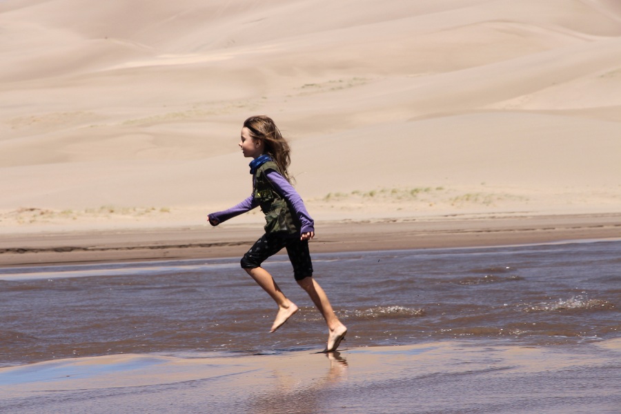 Child running through the seasonal Medano Creek at the base of the dunefield in Great Sand Dunes National Park.