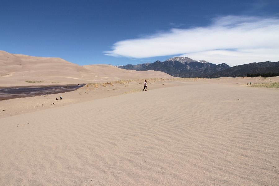 Sandy base of rising dunes split by seasonal Medano Creek, and a view of mountains in the background.