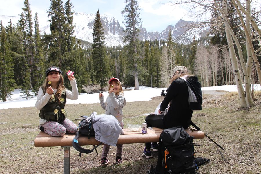 Family sitting on a bench near Wheeler Peak in Great Basin National Park surrounded by snow patches, alpine forest, and mountain scenery after hiking the Lehman Creek Trail.